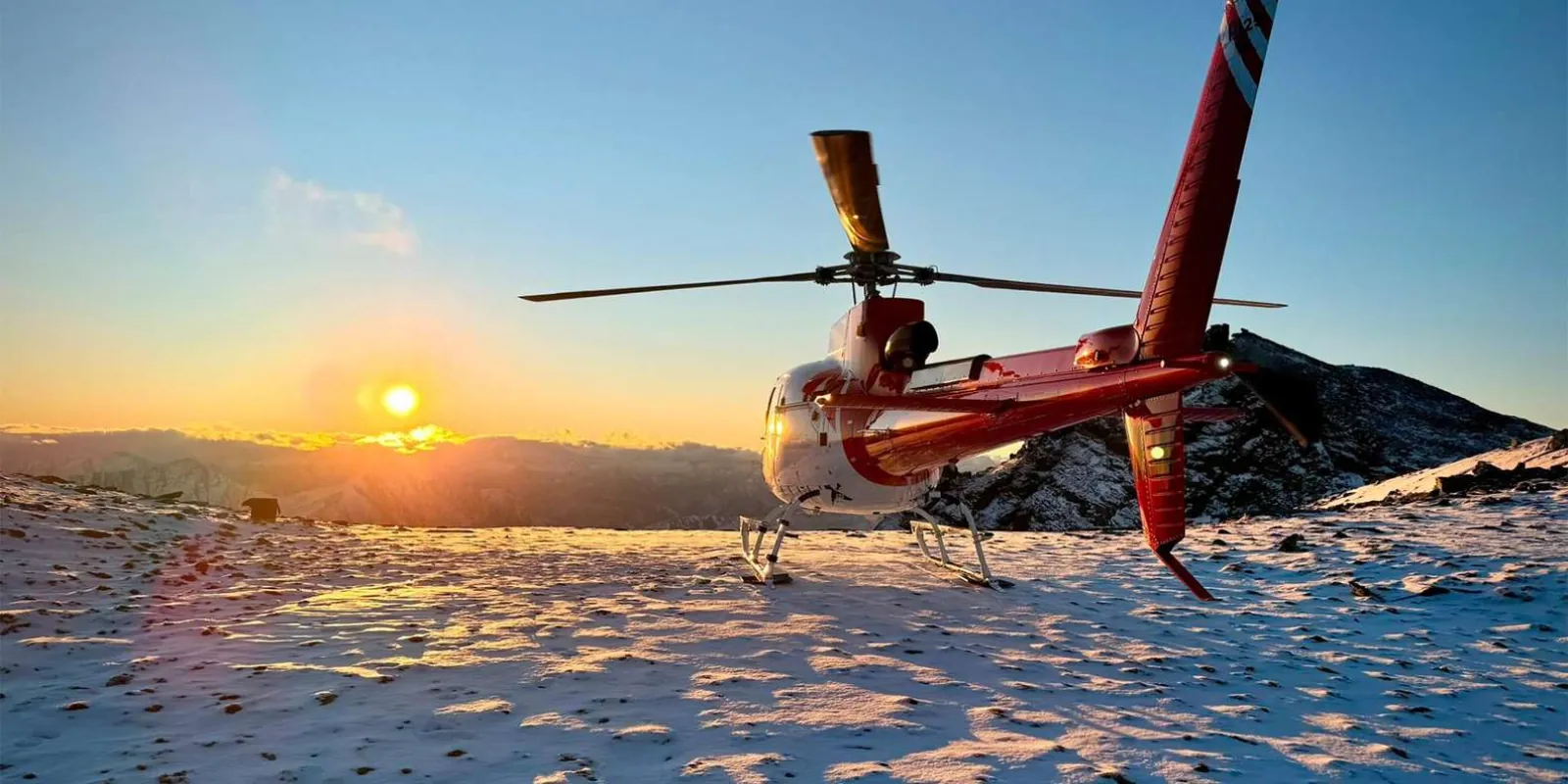 Helicopter shut down on a ridge as the sun drops behind the Southern Alps