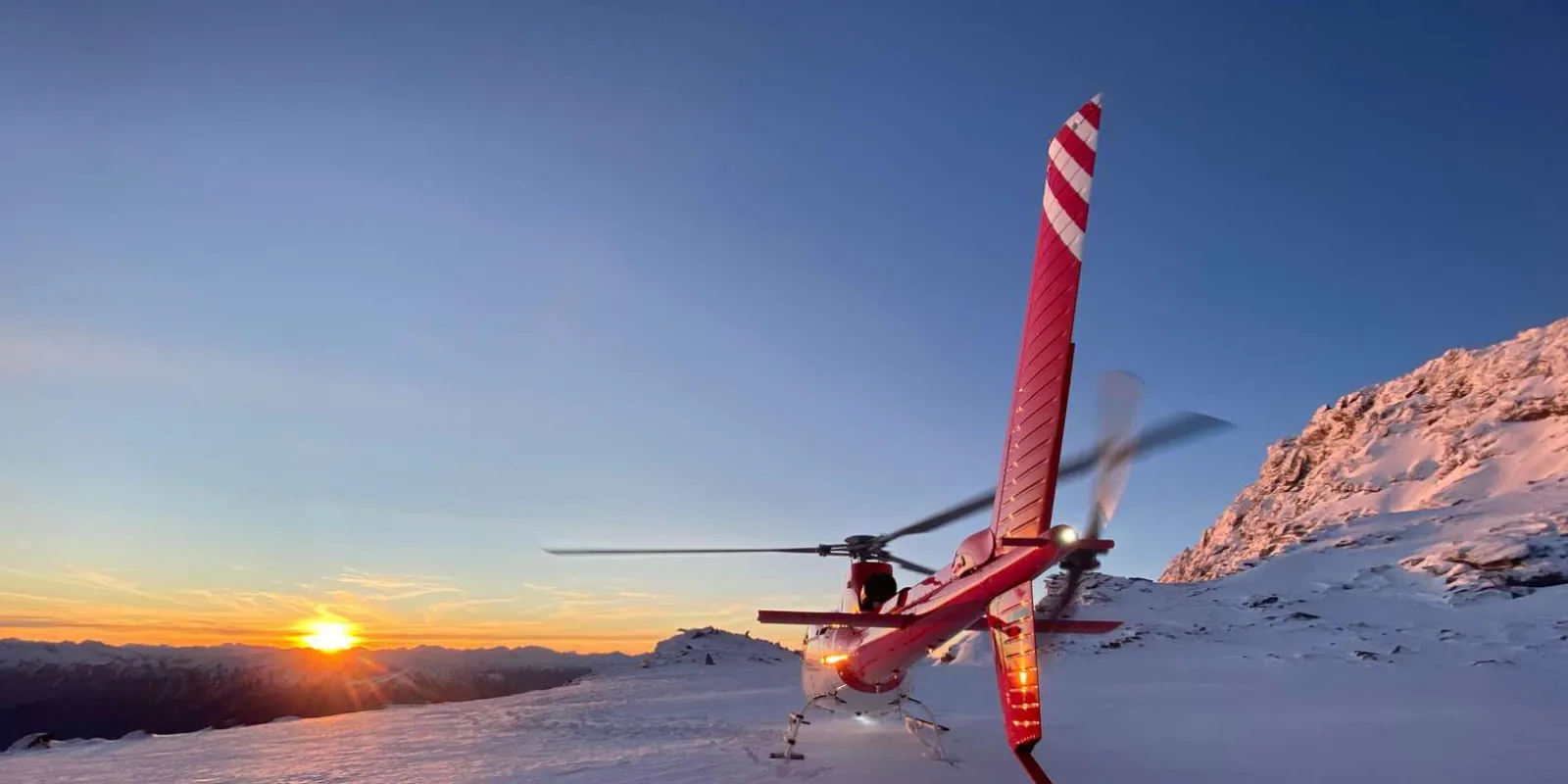 Helicopter silhouetted against an orange and violet sunset sky