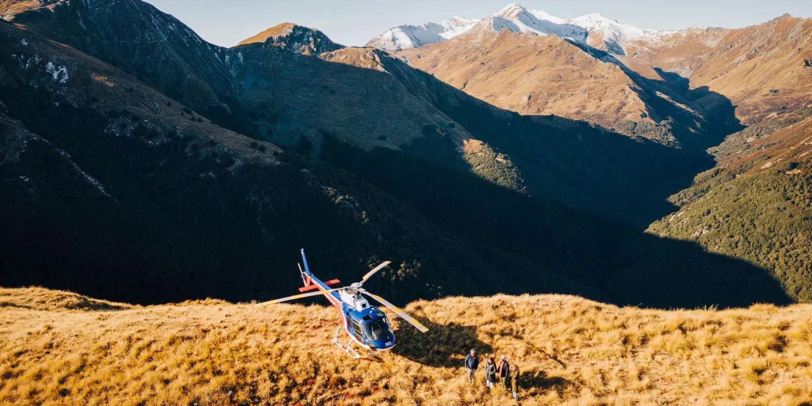 Helicopter tracking low along a golden tussock ridge above the lake