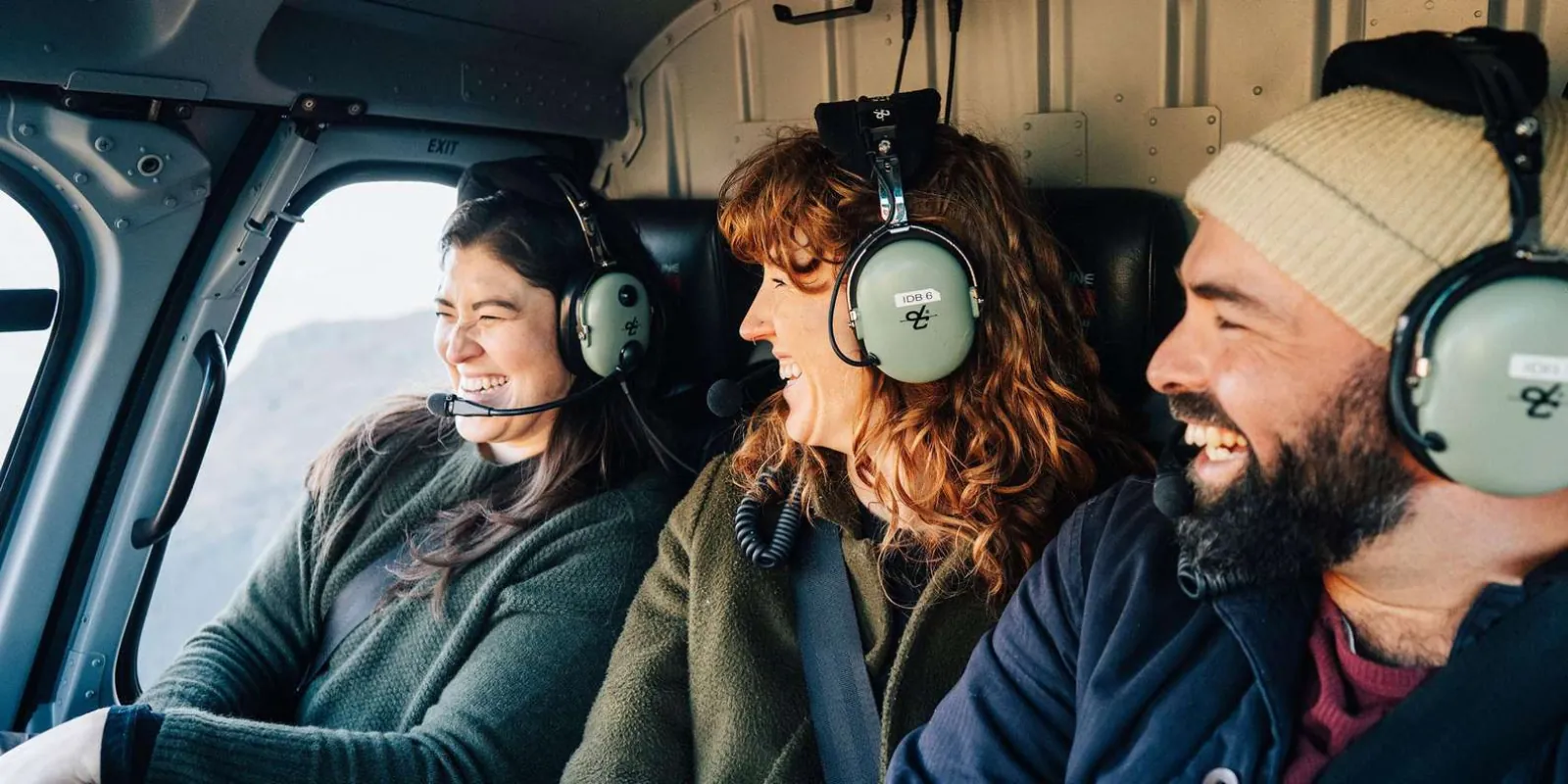 Three passengers in headsets grinning in the helicopter cabin mid-flight