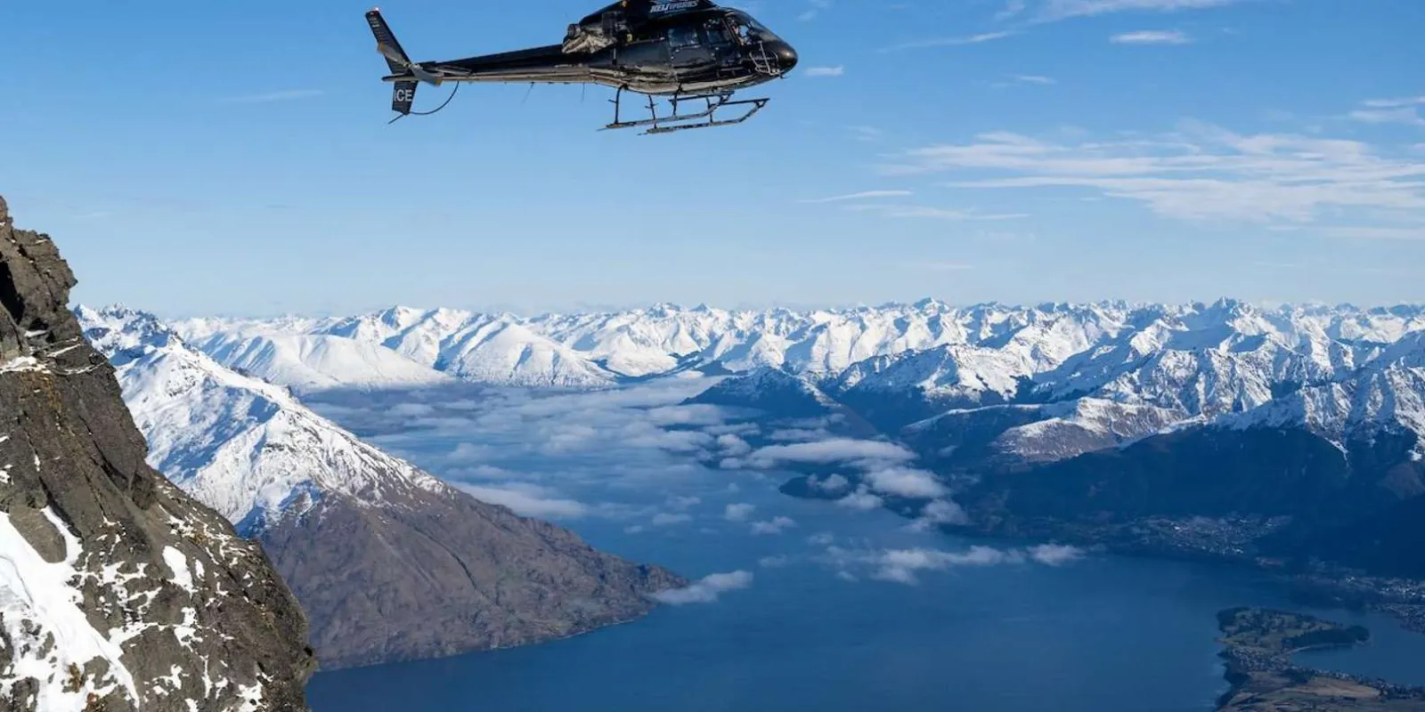 Helicopter crossing Lake Wakatipu with the snowy Remarkables behind