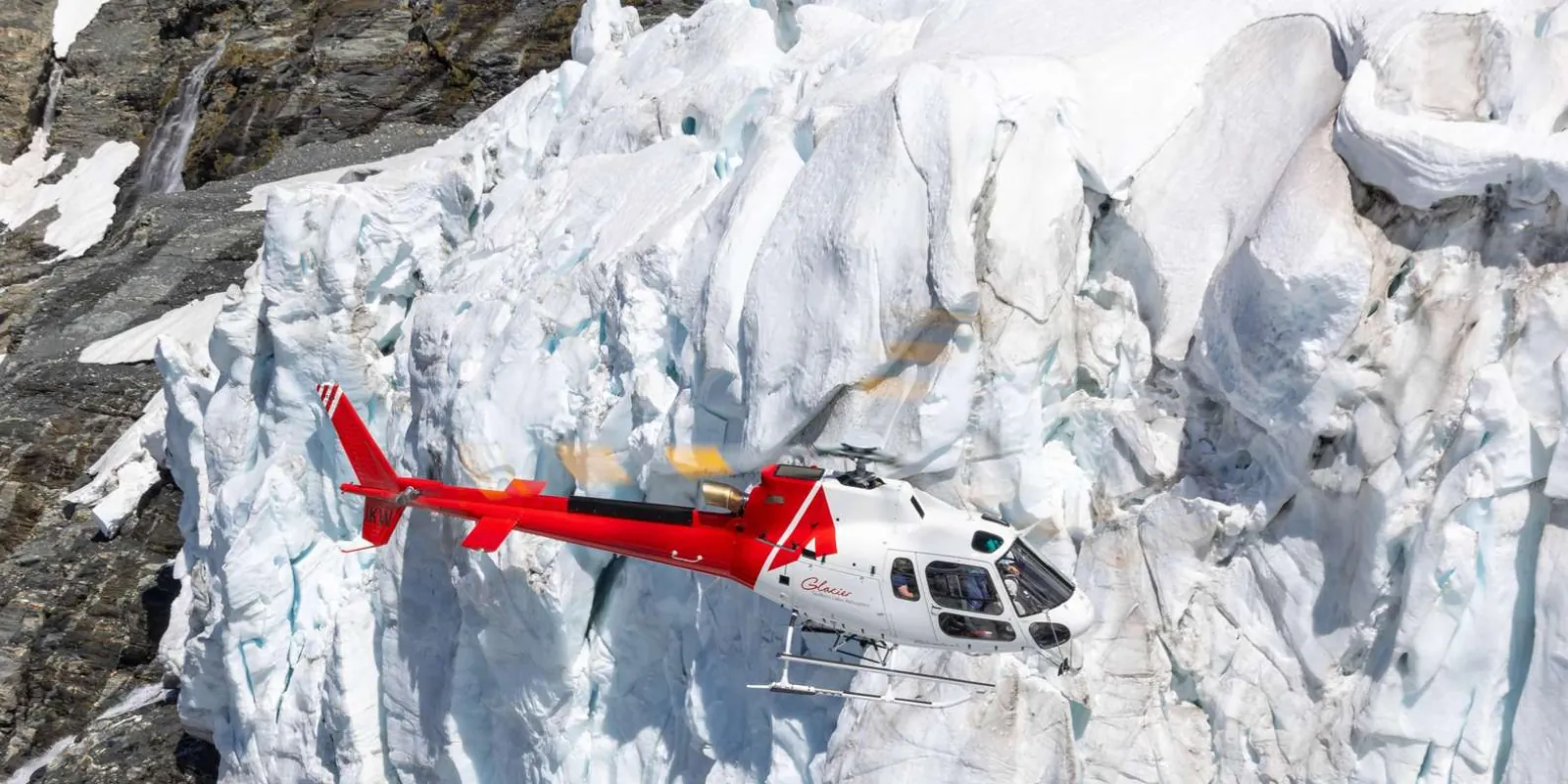 Helicopter parked on the ice beneath a cracked blue glacier face