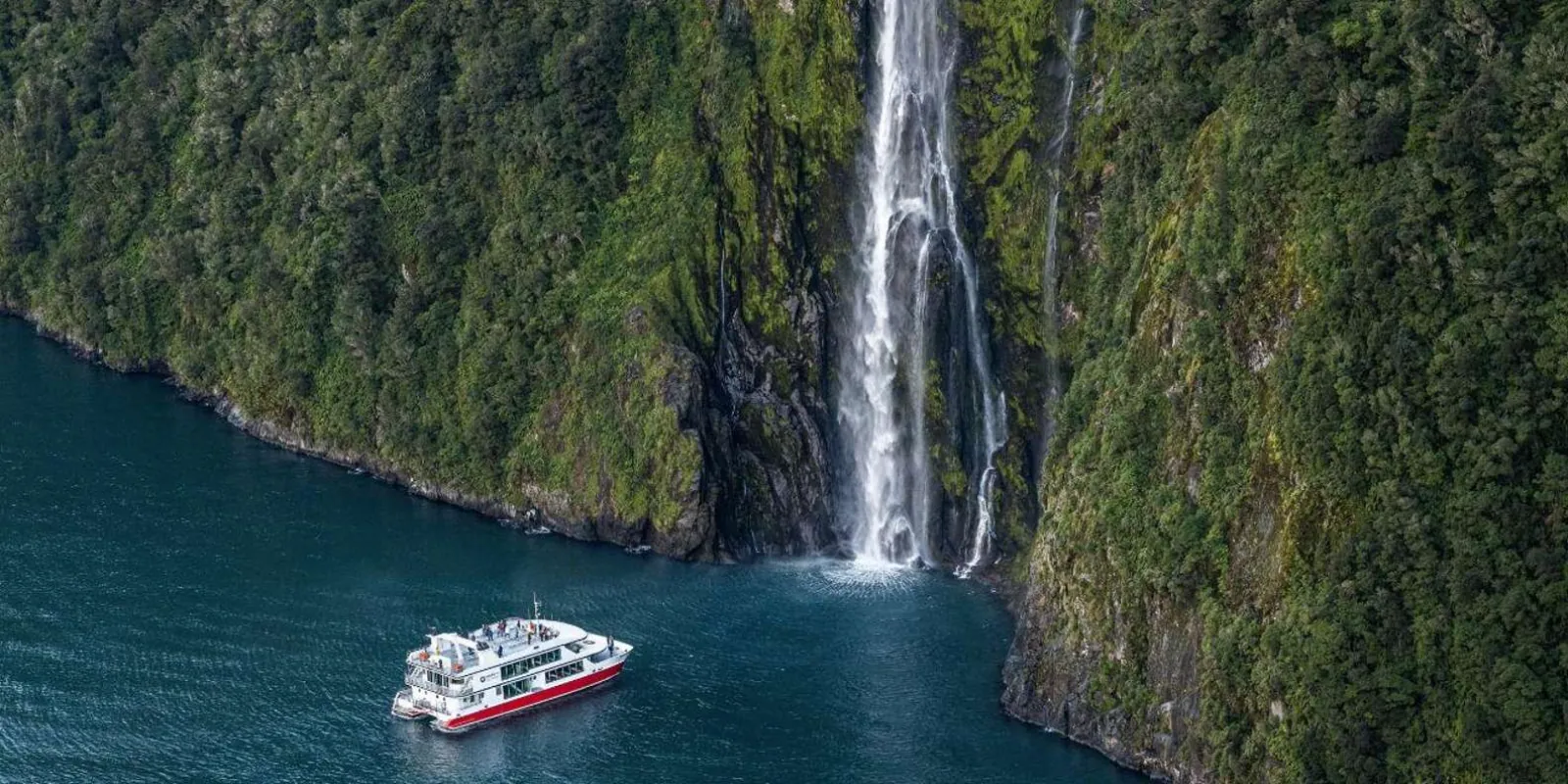 Aerial of the cruise boat nosing toward a waterfall deep in the fiord