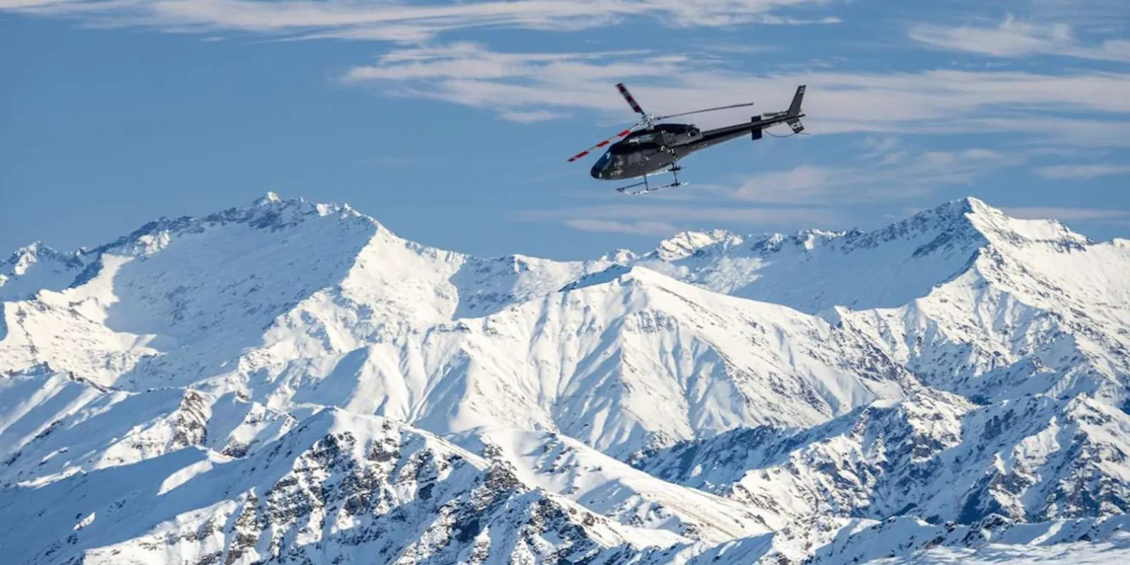 Helicopter crossing a wall of snow-covered peaks under a clear sky