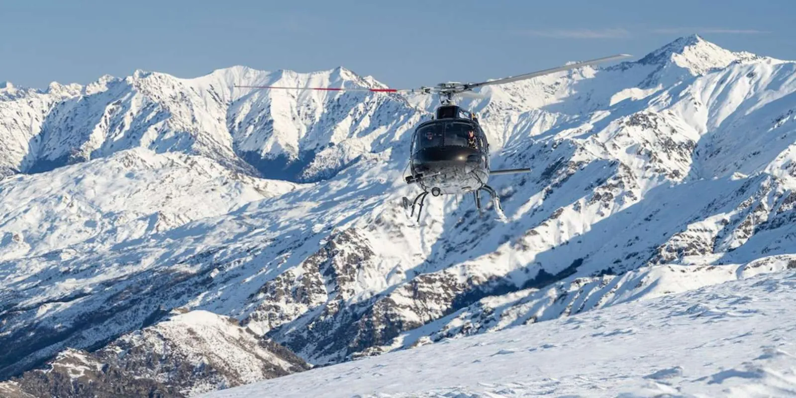 Helicopter descending toward a snowfield ringed by jagged summits